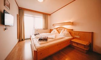 A cozy bedroom with a large wooden double bed. There is a television and large windows that let in plenty of daylight.
