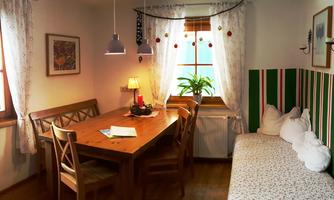 A cozy dining area with a wooden table and chairs. The room is brightly lit and has green walls as well as a windowsill with plants.