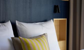 A modern bedroom with two beds and white pillows. The walls are painted blue, and there is a yellow striped decorative pillow.