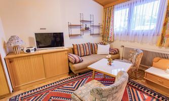 A cozy living room with a comfortable couch and a flat-screen TV. The room has a nice warm light and large windows for plenty of daylight.