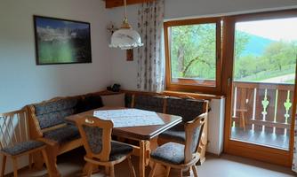 A cozy dining area with wooden furniture and a large window. The view shows a green landscape outside.
