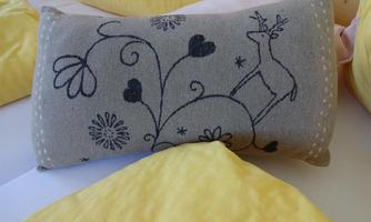 A decorative gray cushion with a deer and floral patterns. In the background, yellow cushions are visible.