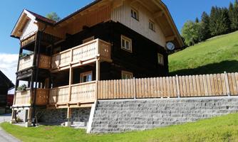 A cozy wooden house with several balconies and a beautiful surroundings. The lawn and landscape are green and inviting.