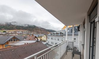 A balcony with a view of a picturesque town and cloudy sky. In the background, mountains are visible, creating a tranquil atmosphere.