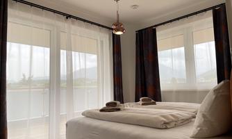 A modern bedroom with a cozy bed and soft curtains. Large windows let in plenty of light and offer a view of the landscape.