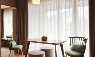 A bright and modern room with a table and two chairs. Large windows with curtains let in plenty of light.