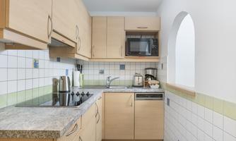 A modern kitchen with wooden cabinets and a granite countertop. It is well-equipped with cooking hobs, a microwave, and a dishwasher.