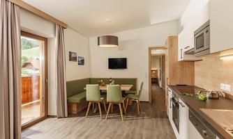 A modern kitchen with a dining area and plenty of natural light. The cozy atmosphere is emphasized by the wood and green tones.