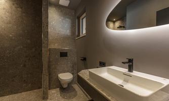 A modern bathroom with gray stone tiles. There is a shower, a sink, and a toilet.