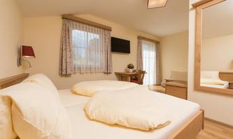 A cozy bedroom with a double bed and large windows. The simply furnished furniture creates an inviting atmosphere.