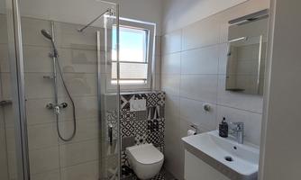 A modern bathroom with a shower, a sink, and a stylish mirror. The walls are in neutral colors, with a patterned tile area.