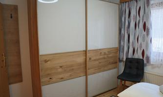 A cozy room with a large wardrobe and a black chair. The windows are decorated with colorful curtains.