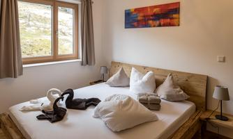 A cozy bedroom with a large bed and several pillows. Well-lit room with a window and a modern piece of art on the wall.