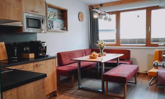 A modern kitchen with a dining area and a large table. The cozy red benches invite you to linger.