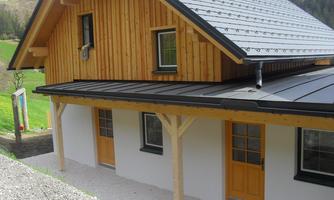 A modern wooden house with a pitched roof. The facade is partially clad in wood and has an inviting front door.