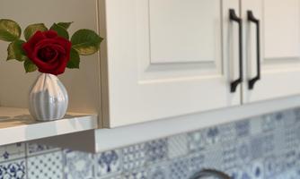 A beautiful red rose in a small vase on a kitchen shelf. In the background, there is a decorative tile with blue and white patterns.