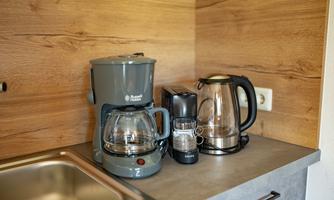 A modern kitchen corner with various electric appliances. Visible are a coffee maker, a kettle, and a blender on a countertop.