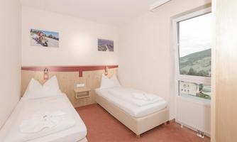 A simple bedroom with two single beds. The room has a window with a view of the landscape and decorative pictures on the walls.