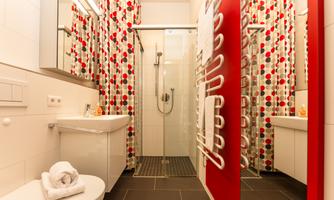 A modern bathroom with a shower cabin and a sink. The walls are designed with colorful curtains and elegant tiles.