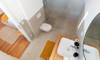 A modern bathroom with stylish tiles and a walk-in shower. The wash area is bright and well-organized, with a large mirror and minimalist accessories.