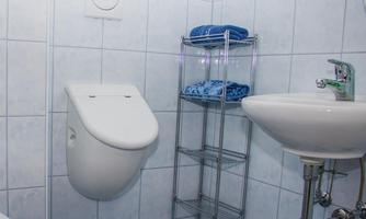 A modern bathroom with white tiles. On the left side, there is a toilet and on the right side, a sink with a towel rack.