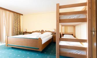 A cozy bedroom with a large double bed and a bunk bed. The room has bright walls and plenty of daylight.