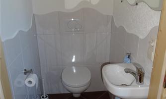 A small, bright bathroom with a toilet and a small sink. The walls are tiled and there is a mirror.