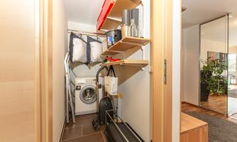 A small utility room with a washing machine and shelves. Various utensils and cleaning supplies are neatly stored.