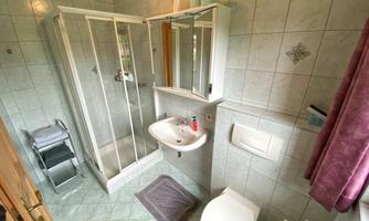 A bright bathroom with tiled walls and a shower. There is a sink, a toilet, and some towels.