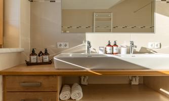 A modern bathroom with a large sink and a mirror. On the shelf are care products and fresh towels.