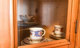 A glass display case with fine china. Inside, there are various cups and saucers made of porcelain.