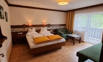 A cozy hotel room with a double bed and a sofa bed. The large windows let in plenty of light and offer a view of the balcony.
