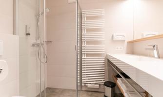 A modern bathroom with a shower, a sink, and a towel radiator. The walls are light and the decor is simple and functional.