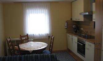 A cozy kitchen with a dining table and chairs. The walls are in soft colors, and plenty of light falls through the window.