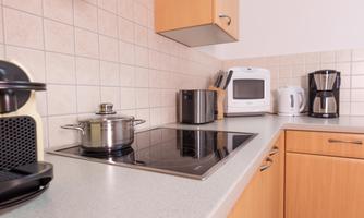 A modern kitchen with light wood cabinets and various appliances. On the countertop are a pot, a microwave, and a coffee machine.