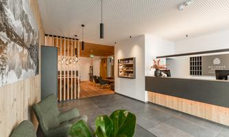 A modern reception area with wooden details and cozy seating. In the background, there is a large art wall depicting a natural landscape.