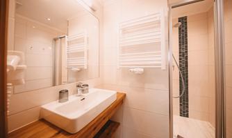A modern bathroom with a sink on a wooden table and a glass shower cubicle. The walls are light and designed in a minimalist style.