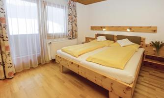 A cozy bedroom with a double bed and yellow blankets. Large windows provide plenty of daylight and a pleasant atmosphere.