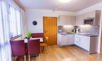 A modern kitchen with a dining table and red chairs. The space is designed to be bright and welcoming.