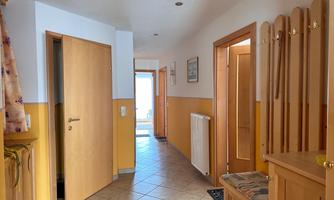 A bright hallway with various doors and tiled flooring. Decorative pictures are hanging on the wall, and a coat rack is visible.