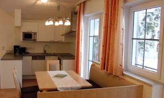 A modern kitchen with a dining area. Large windows let in plenty of light and offer a view of nature.