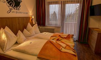 A cozy bedroom with a double bed and large pillows. Large windows let in plenty of daylight, and the walls are tastefully decorated.