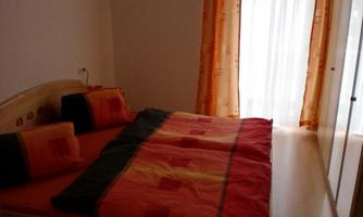 A cozy bedroom with a large bed and colorful blankets. Bright curtains hang in front of the window, letting light in.