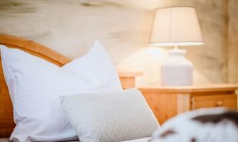 A cozy bedroom with a wooden bed frame and comfortable pillows. Next to the bed, there is a lamp on a nightstand.