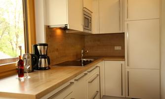 A modern kitchen with white cabinets and a wooden countertop. It is brightly lit and features a coffee machine and a sink.