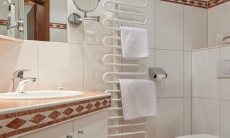 A modern bathroom with a sink, a mirror, and a heated towel rack. The walls are tiled, and there is a toilet in the corner.
