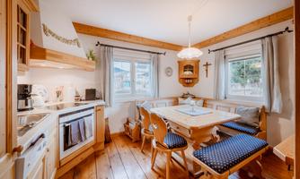 A cozy kitchen with wooden details and a dining area. There is a table with benches and windows that let in natural light.