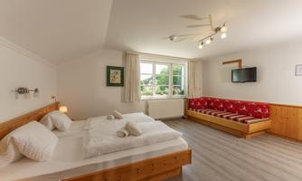 A bright room with two beds and a seating area. Large windows provide plenty of daylight and a view.