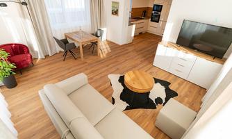 A modern living room with a comfortable sofa and a round coffee table. The apartment has large windows and a bright, friendly atmosphere.