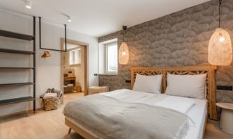 A modern bedroom with a large double bed and stylish light fixtures. The walls are decorated, and there is a shelf for storage.